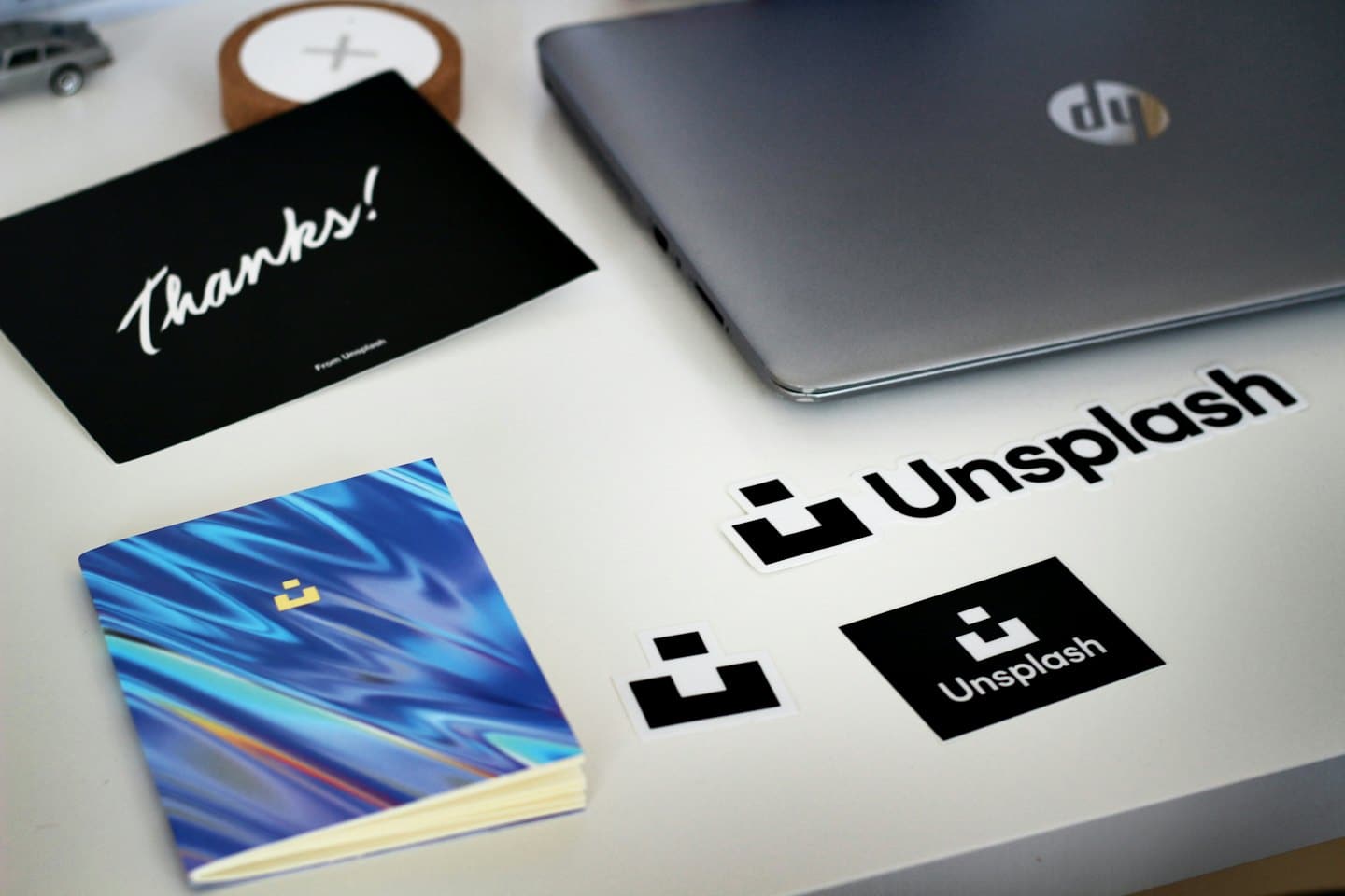Na bielom stole sú naaranžované nálepky na notebooky a zápisníky s logom.